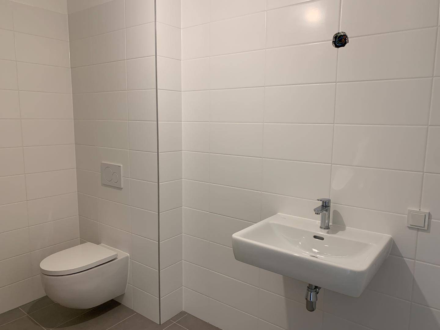 Modernes Gäste-WC mit wandhängendem WC und kleinem Waschbecken, hell gefliest und sauber.