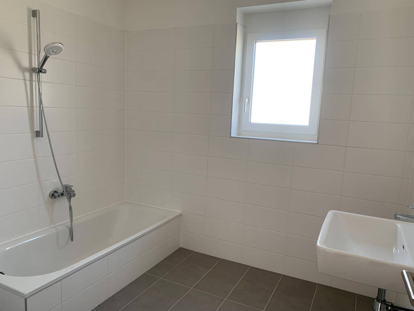 Modernes Badezimmer mit Badewanne, Dusche und Waschbecken, hell gefliest und funktional gestaltet.