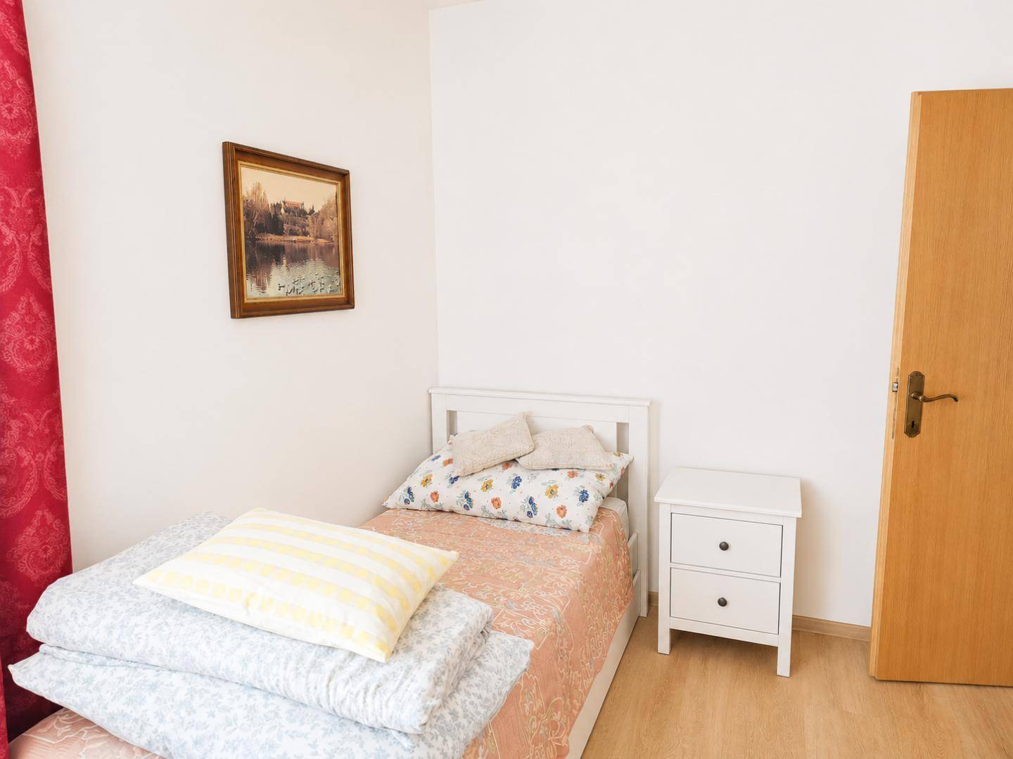 Kleines Schlafzimmer mit Einzelbett, Nachttisch und schlichter Einrichtung, ideal als Gästezimmer.