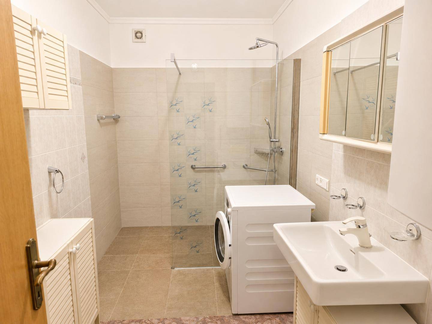 Helles Badezimmer mit barrierefreier Dusche, Waschmaschine und praktischem Spiegelschrank.