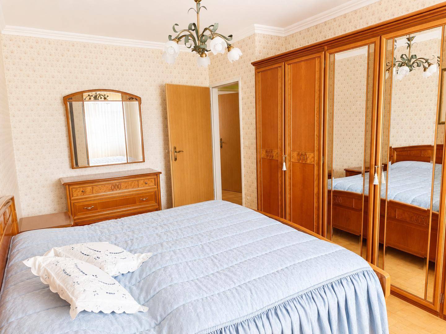 Schlafzimmer mit Doppelbett, Spiegelschrank und Kommode, eingerichtet in einem traditionellen Stil.