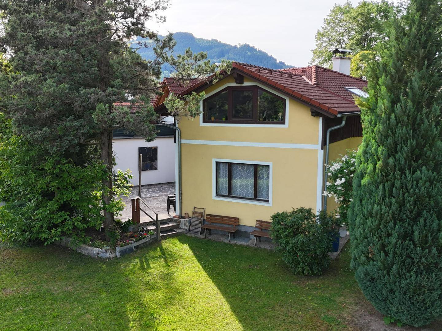 Ansicht des gelben Hauses mit rotem Ziegeldach, umgeben von Bäumen und einem gepflegten Rasen.