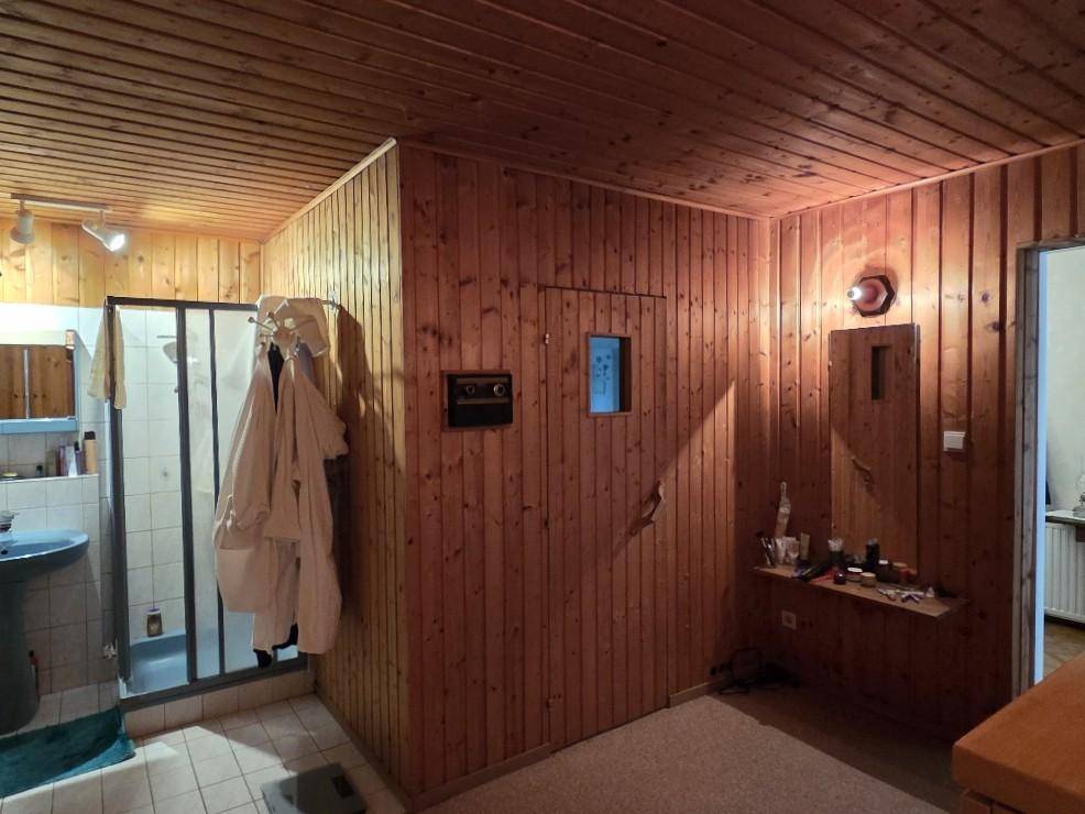 Badezimmer mit Holzverkleidung, Duschkabine und Waschbecken, möglicherweise Teil eines Wellnessbereichs.