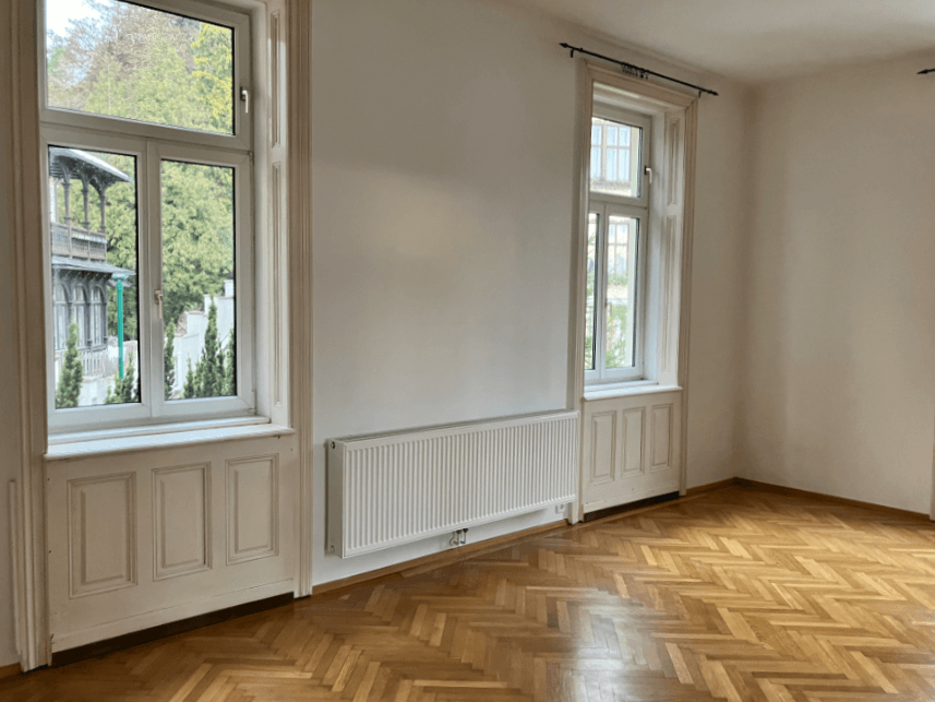 Leeres Zimmer mit Fischgrätparkett und hohen Fenstern, bereit zur individuellen Gestaltung.