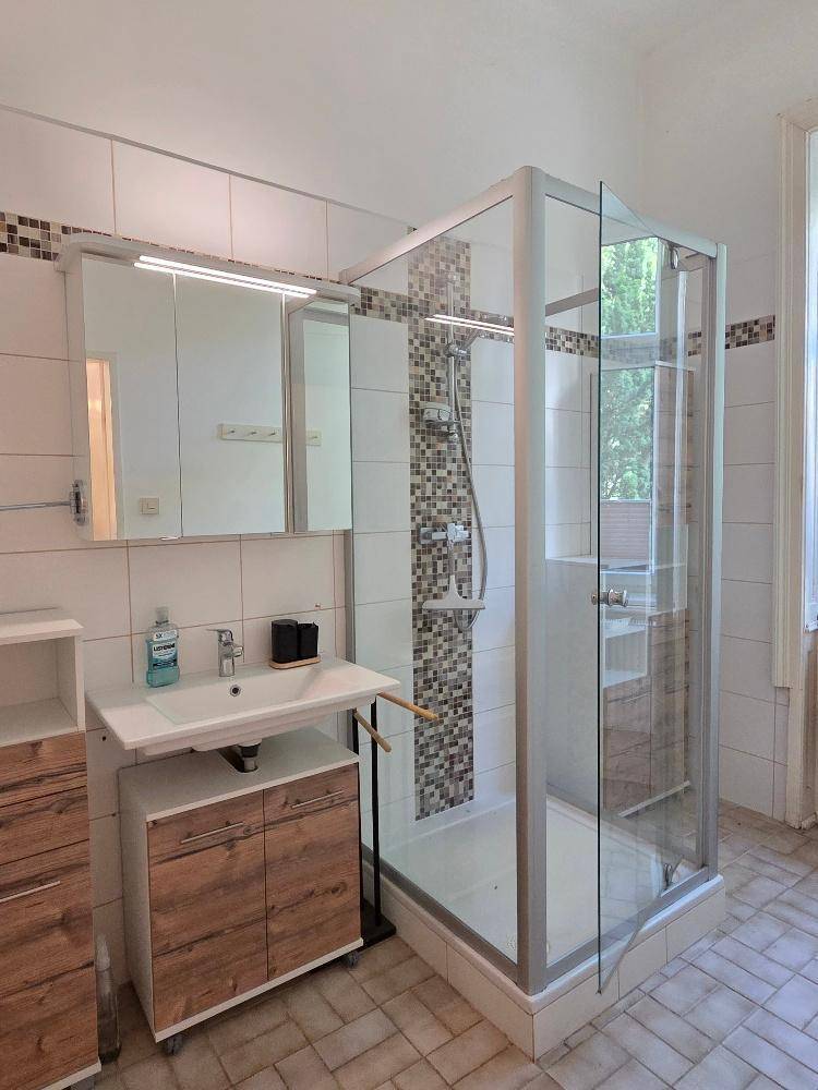 Badezimmer mit Duschkabine, Einzelwaschbecken und hellen Fliesen, funktional eingerichtet.