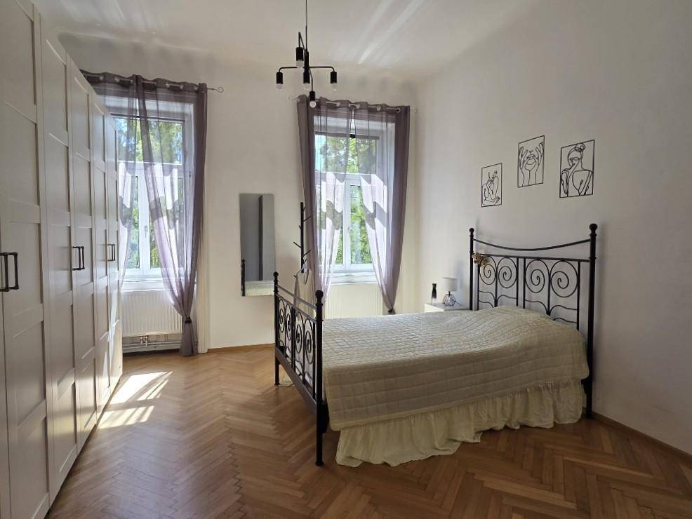 Schlafzimmer mit Fischgrätparkett, schmiedeeisernem Bett und großen weißen Kleiderschränken.