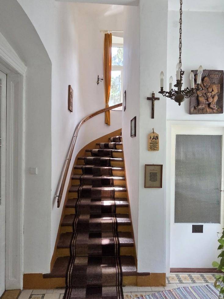 Geschwungene Treppe mit gemustertem Teppichläufer und Holzgeländer, führt in die oberen Stockwerke.