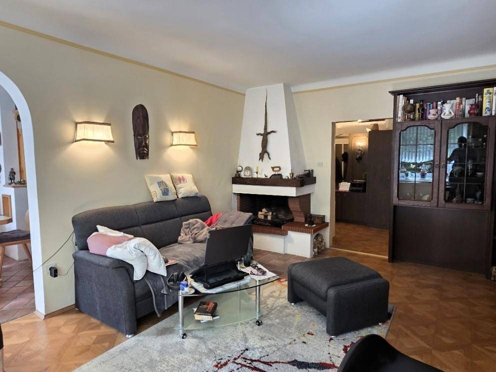 Gemütliches Wohnzimmer mit Kamin, Sofa und Parkettboden, offen zu einem weiteren Raum.