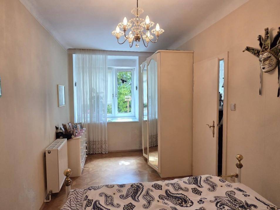 Schlafzimmer mit Doppelbett, Kleiderschrank und Fenster, beleuchtet von einem Kronleuchter.