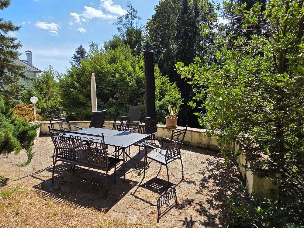 Geräumige Terrasse mit Gartenmöbeln, umgeben von üppigem Grün und Bäumen.