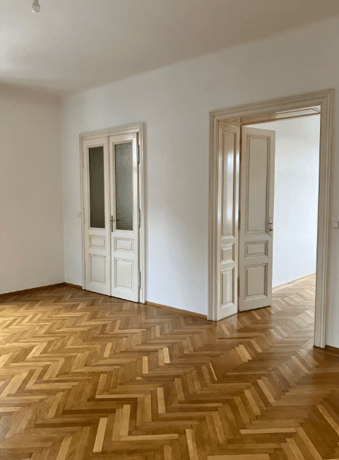 Geräumiges leeres Zimmer mit Fischgrätparkett und zwei Türen, bietet vielseitige Nutzungsmöglichkeiten.