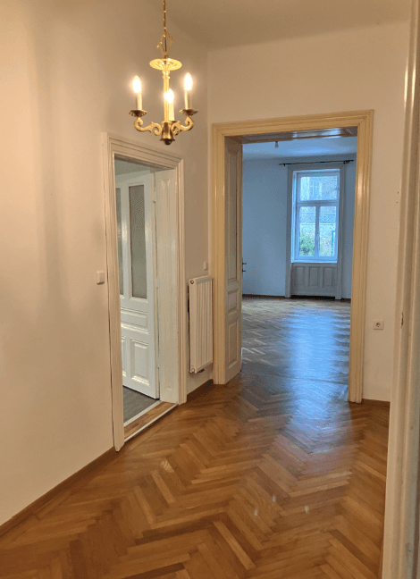 Heller Flur mit glänzendem Fischgrätparkett und klassischem Kronleuchter, verbindet die Zimmer.