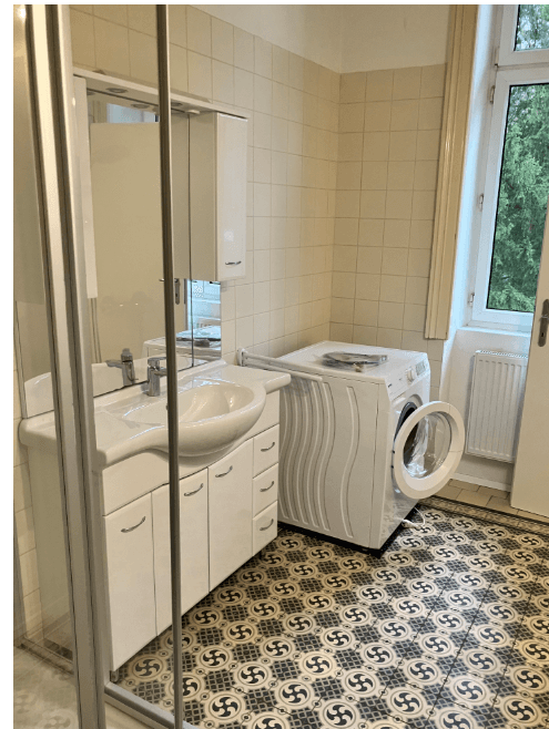 Badezimmer mit auffälligen Fliesen, Einzelwaschbecken, Duschkabine und integrierter Waschmaschine.