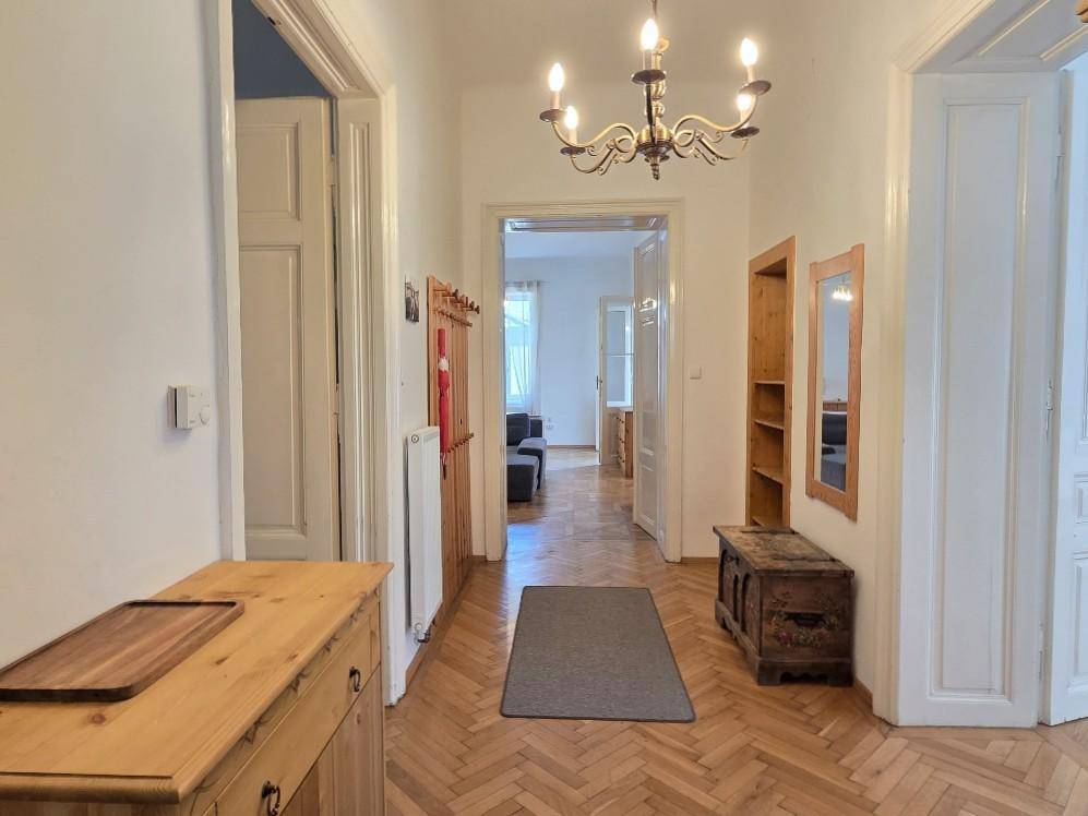 Heller Flur mit Fischgrätparkettboden, Holzmöbeln und einem eleganten Kronleuchter.