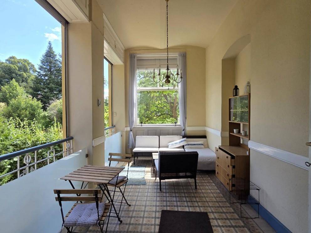 Helle Loggia mit Fliesenboden, Sitzgelegenheiten und einem schönen Blick ins Grüne.