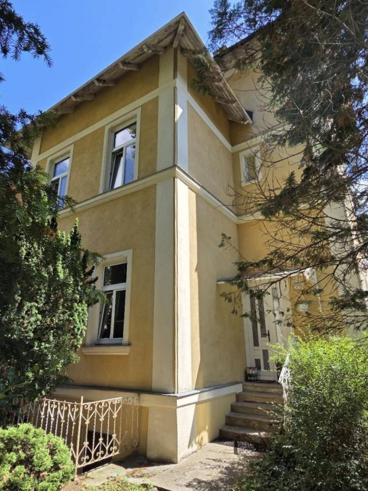 Eckansicht des Gebäudes mit gelber Fassade, weißen Fensterrahmen und Eingangsbereich.