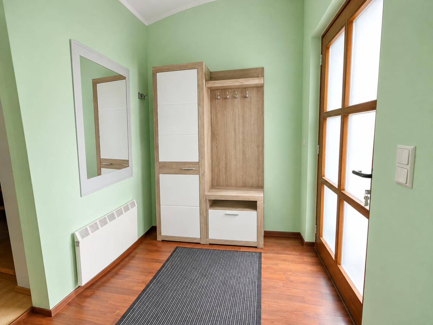 Heller Eingangsbereich mit Garderobe, Spiegel und Fenster zur Außenseite.