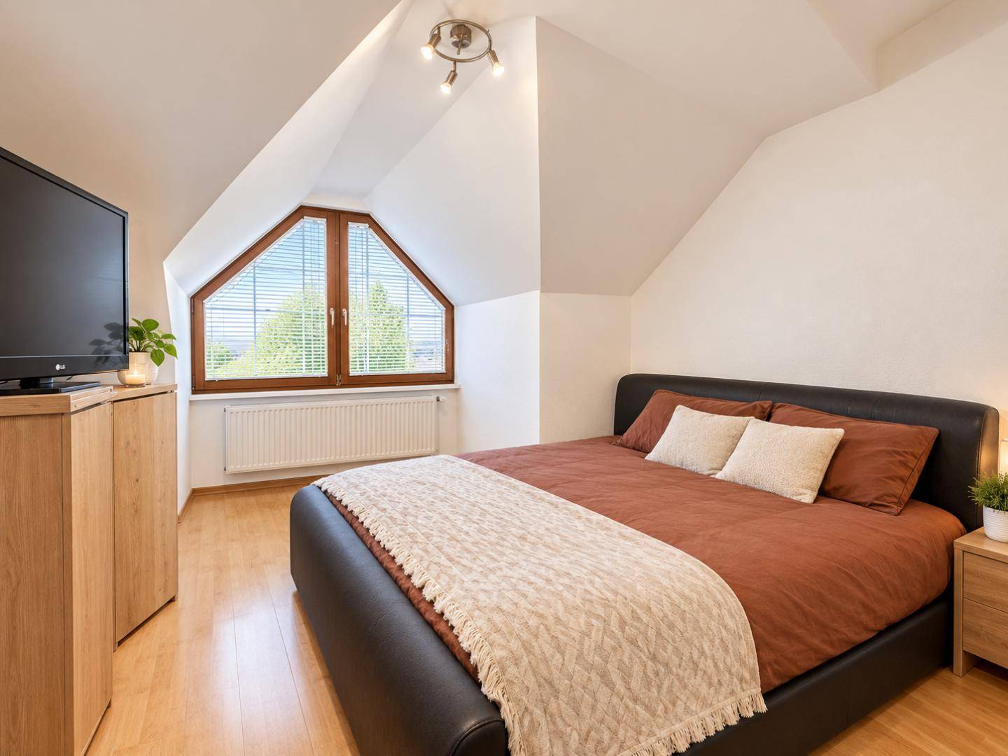 Helles Schlafzimmer im Dachgeschoss mit Doppelbett, Fernseher und schrägen Wänden.
