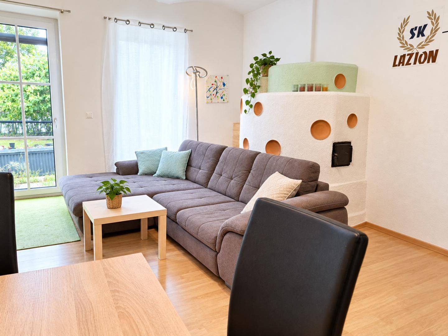 Gemütliches Wohnzimmer mit großem Sofa, Kachelofen und Zugang zum Außenbereich.