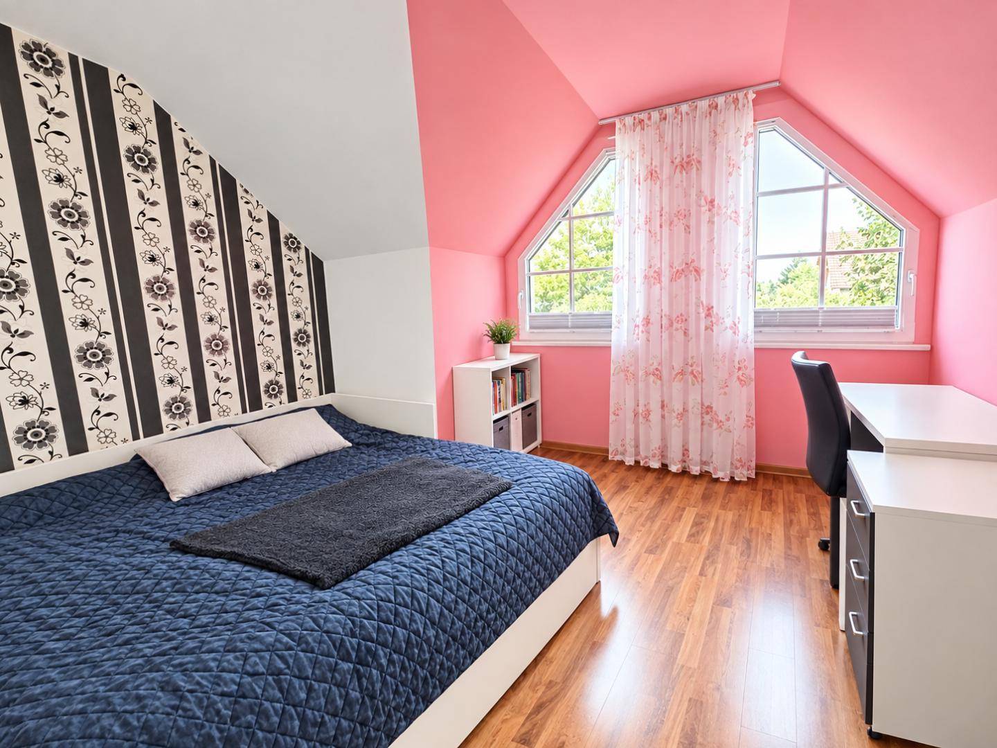 Schlafzimmer im Dachgeschoss mit schräger Decke, floraler Tapete und großem Fenster.