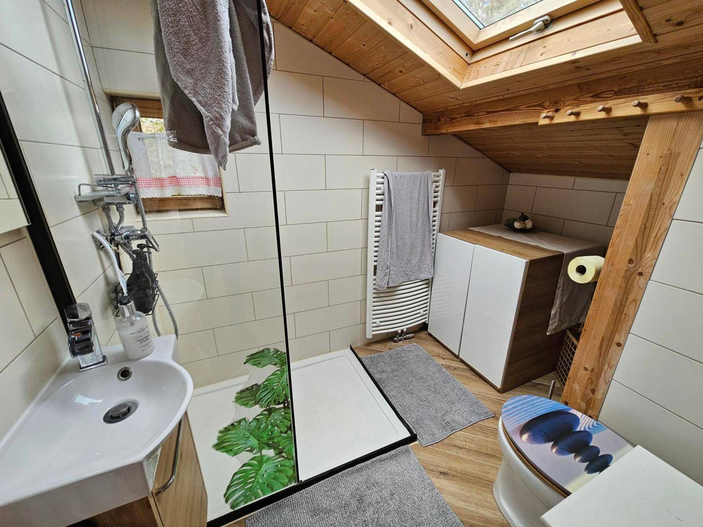 Modernes Badezimmer im Dachgeschoss mit begehbarer Dusche, Dachfenster und Holzelementen.