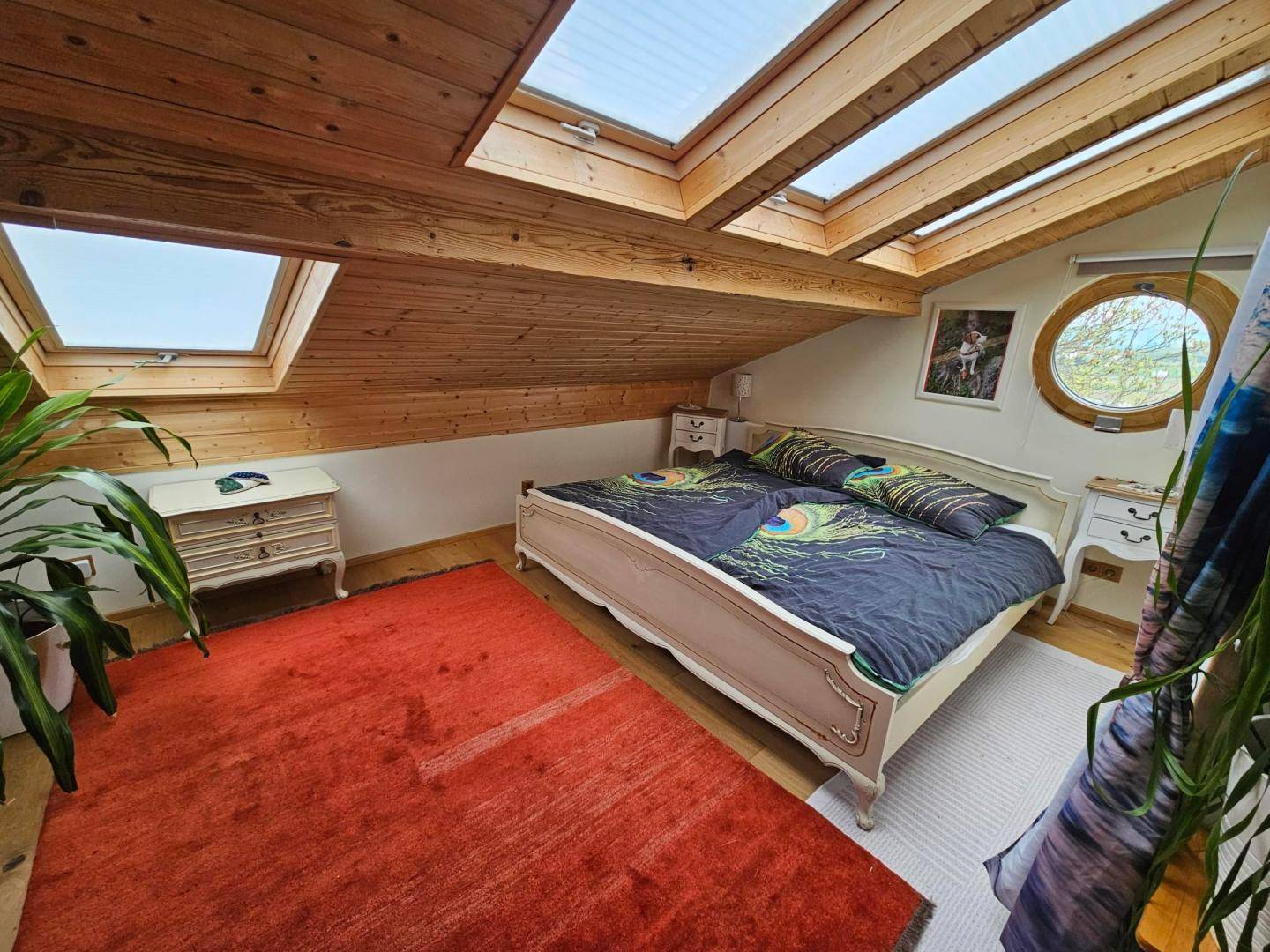 Gemütliches Schlafzimmer im Dachgeschoss mit Holzbalken, Dachfenstern und einem runden Fenster.