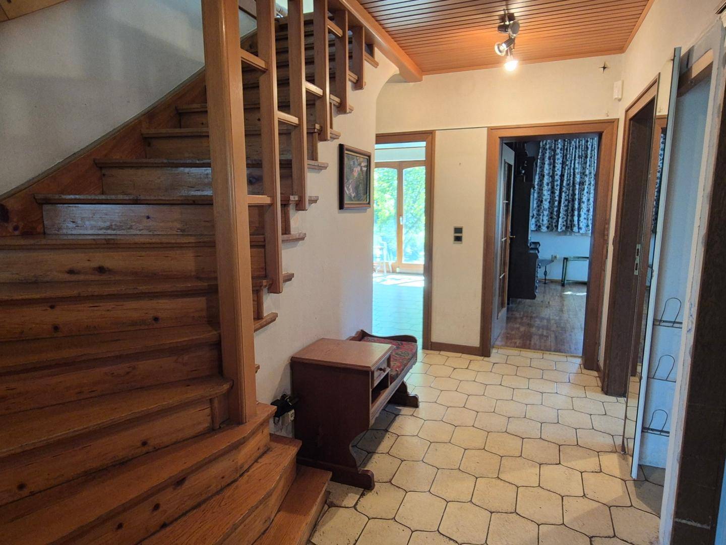Heller Flur mit Holztreppe, Fliesenboden und Zugang zu weiteren Räumen im Haus.