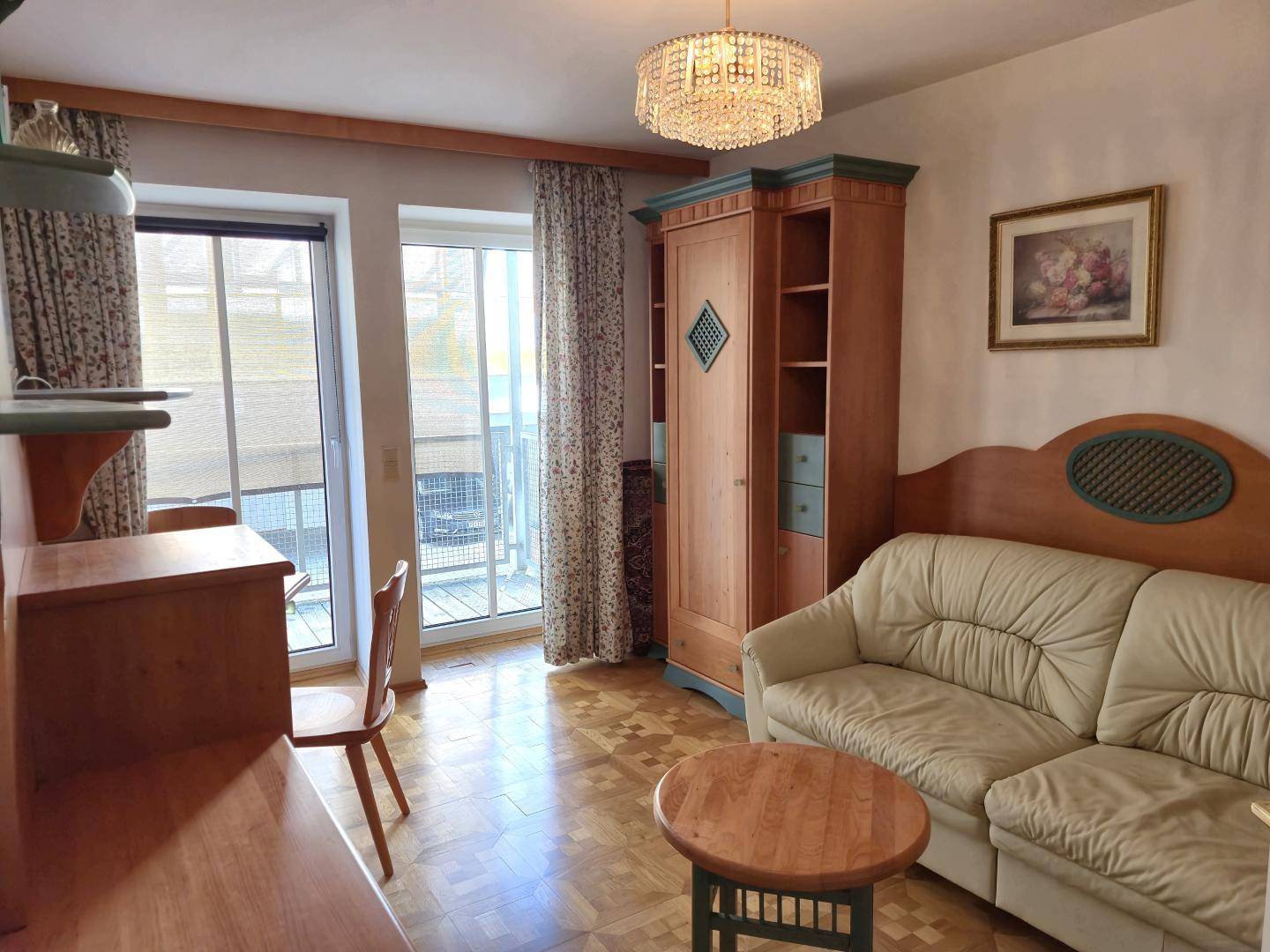 Gemütliches Zimmer mit Sofa, Schrank, Schreibtisch und Balkonzugang.