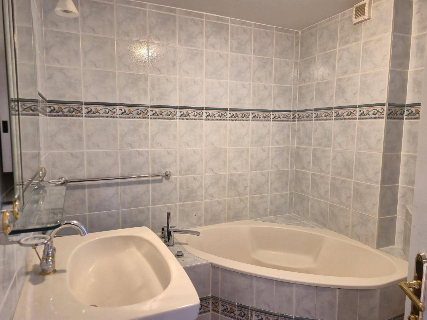 Badezimmer mit hellgrauen Fliesen, Eckbadewanne und Einzelwaschbecken.