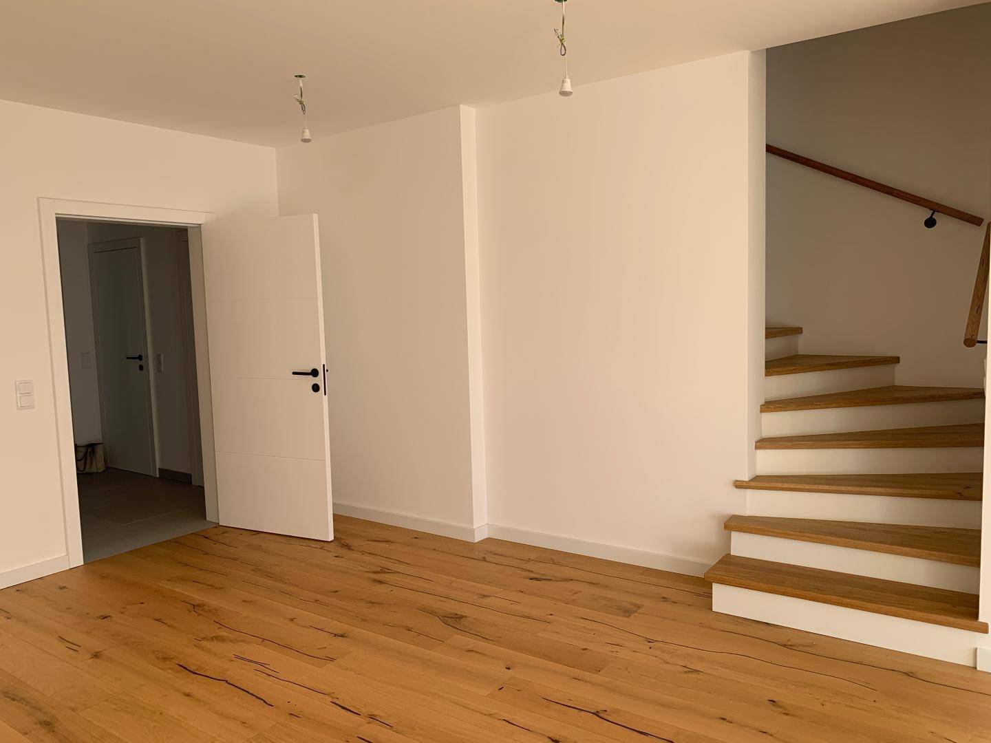 Heller Flur mit Holztreppe und weißer Tür, die zu weiteren Räumen führt.