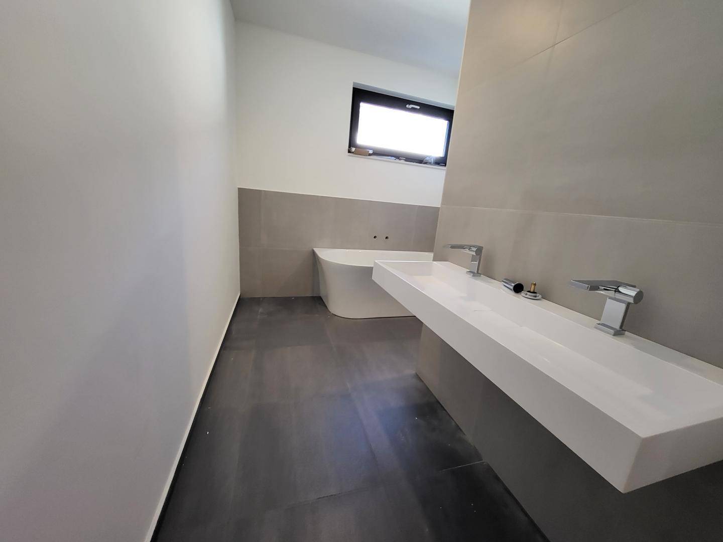 Modernes Badezimmer mit freistehender Badewanne, langem Waschbecken und Fenster.
