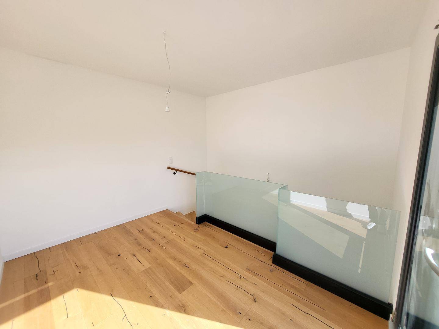 Heller Bereich im Obergeschoss mit Holzboden und modernem Glasgeländer.