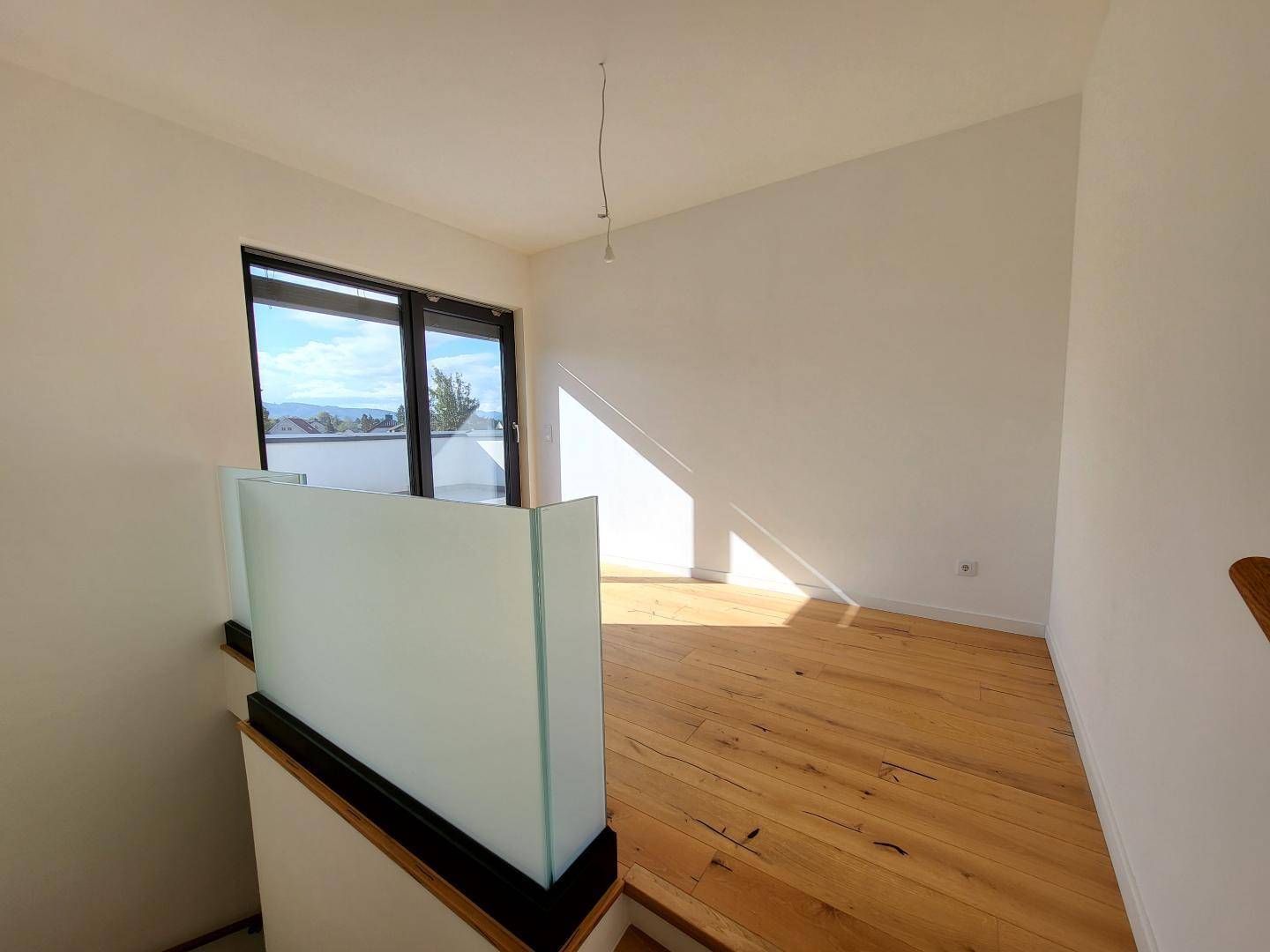Heller Flur im Obergeschoss mit Holzboden, Glasgeländer und Zugang zur Dachterrasse.