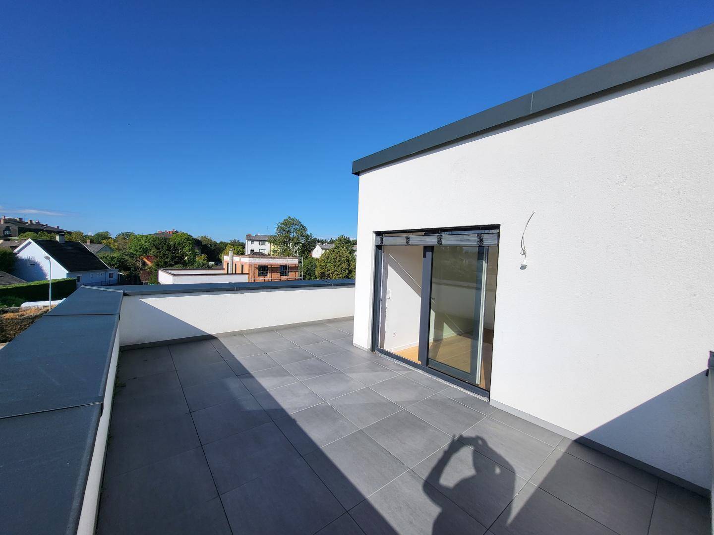 Weitläufige Dachterrasse mit grauen Fliesen und Blick auf die umliegenden Häuser.