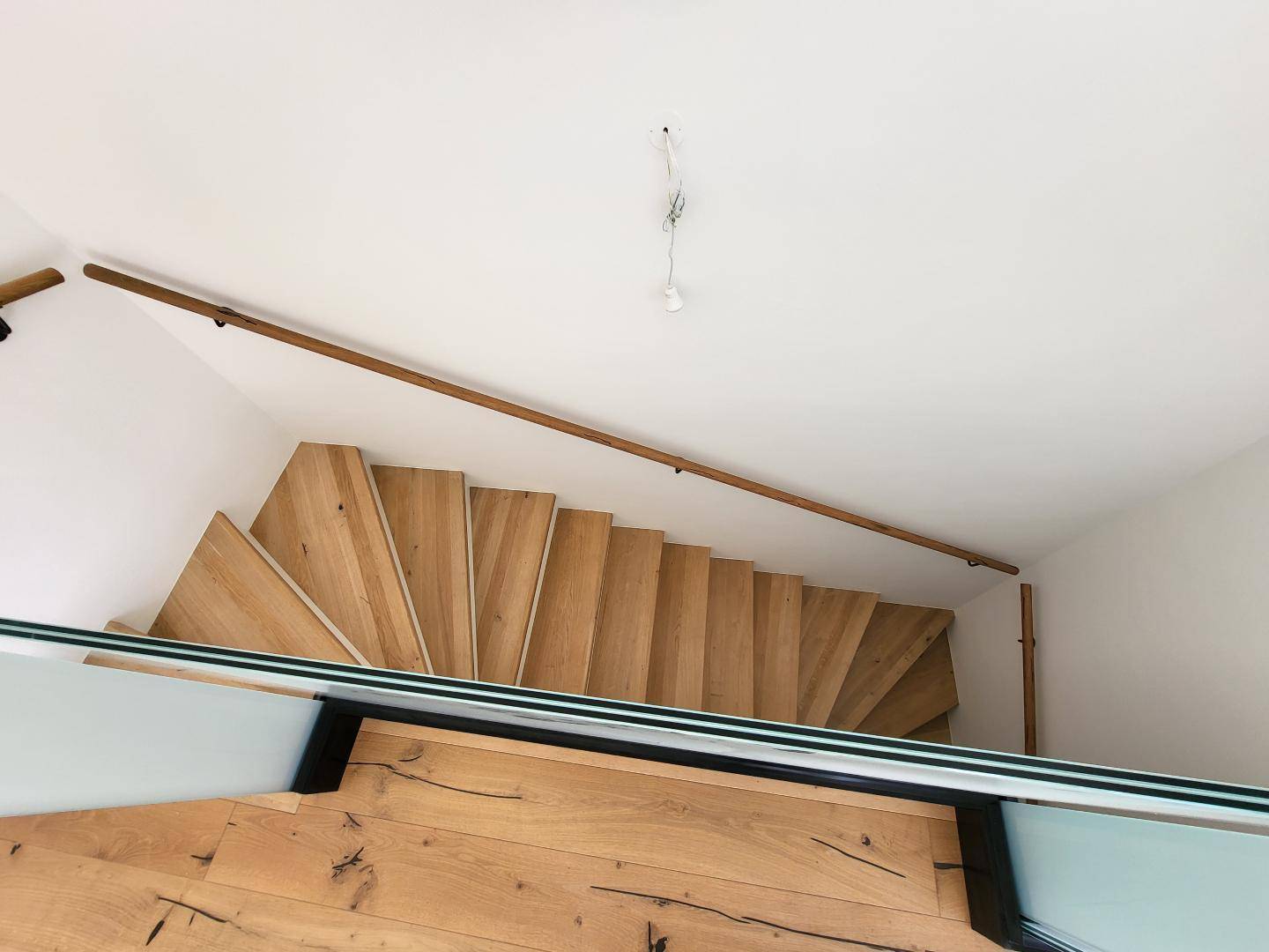 Blick von oben auf eine moderne Holztreppe mit elegantem Glasgeländer.