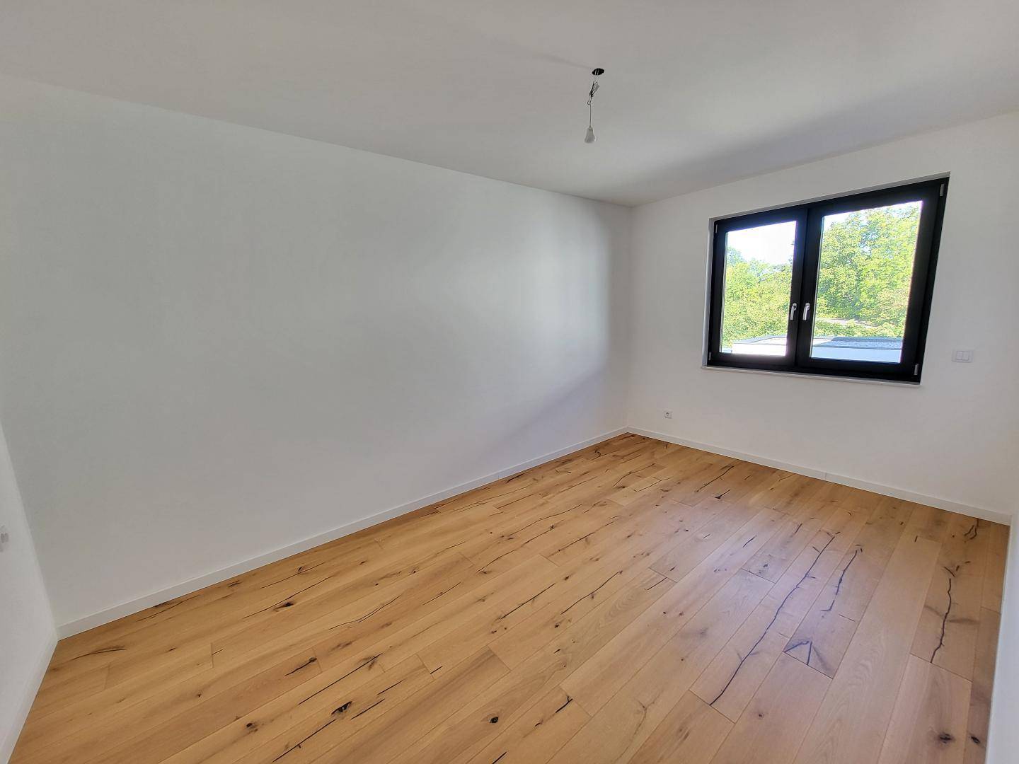 Helles Schlafzimmer mit Holzboden und Blick ins Grüne durch das Fenster.