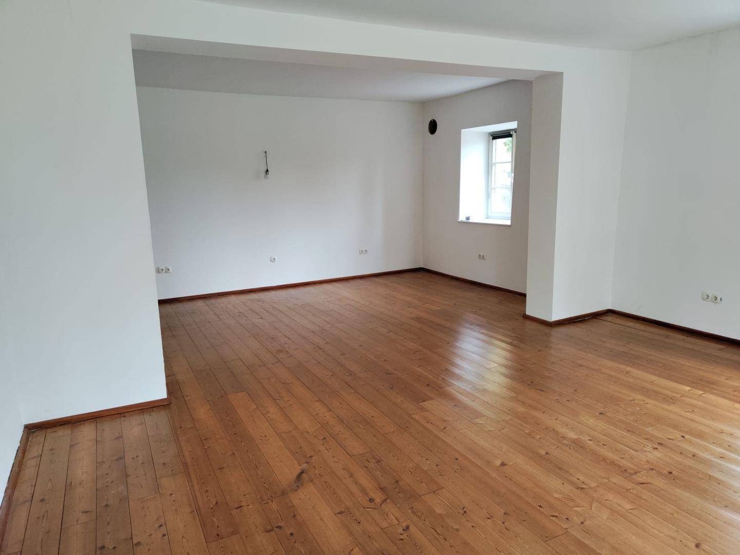 Geräumiges, leeres Wohnzimmer mit Holzdielenboden und weiß gestrichenen Wänden.