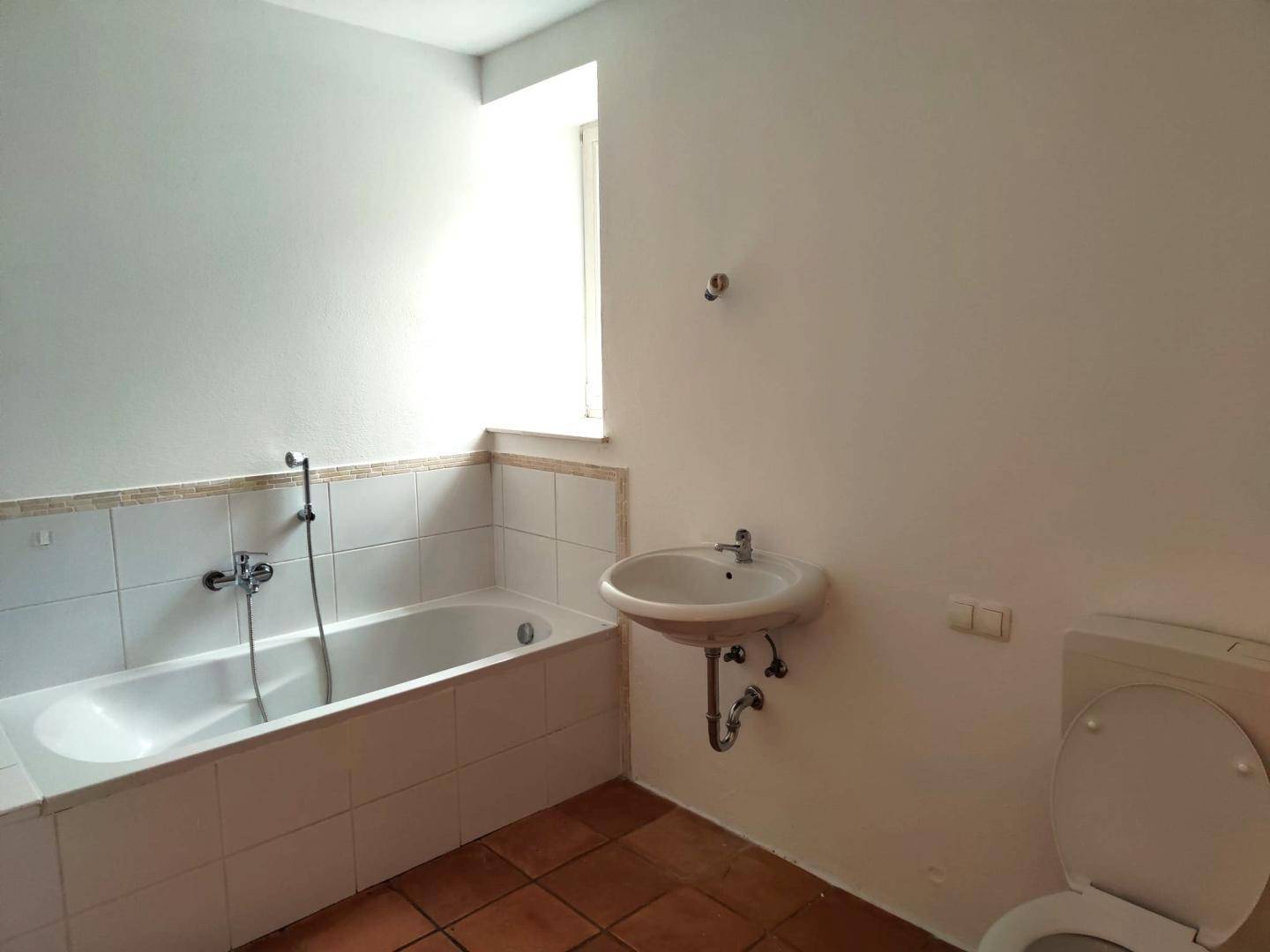 Badezimmer mit Badewanne, Waschbecken und WC, ausgestattet mit Terrakottafliesen.