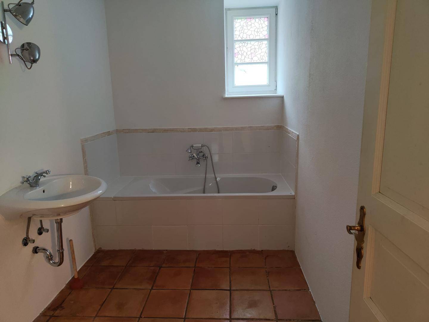 Badezimmer mit Badewanne, Waschbecken und Fenster, ausgestattet mit Terrakottafliesen.