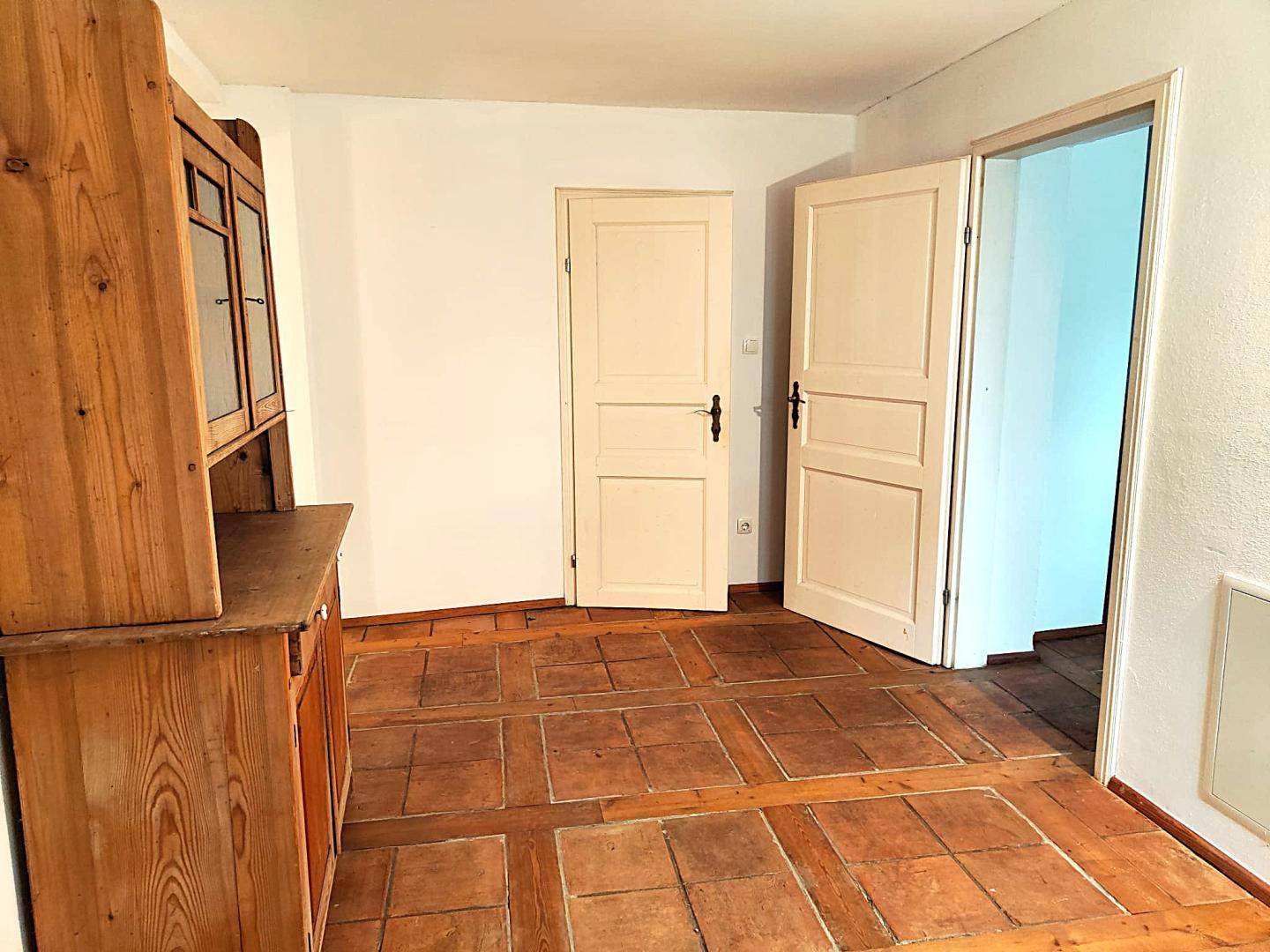 Raum mit Terrakottafliesen und Holzdielen, ausgestattet mit einem rustikalen Holzschrank.