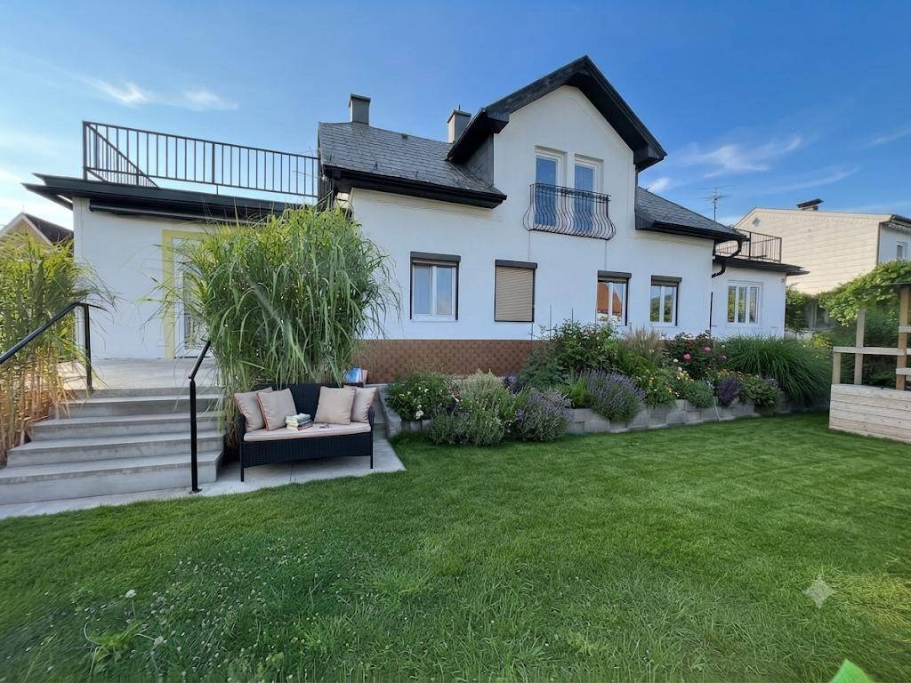 Gepflegter Garten mit Rasenfläche, Blumenbeeten und einer gemütlichen Sitzbank vor dem Haus.