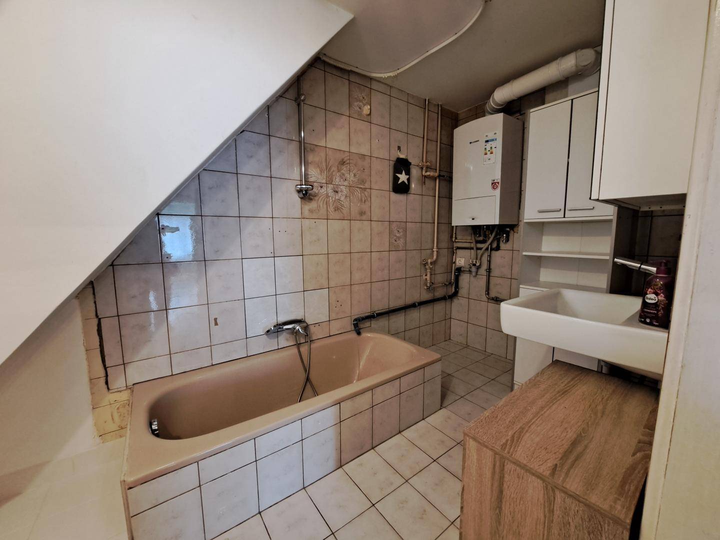 Badezimmer mit Badewanne, Waschbecken und Gastherme unter einer Dachschräge.