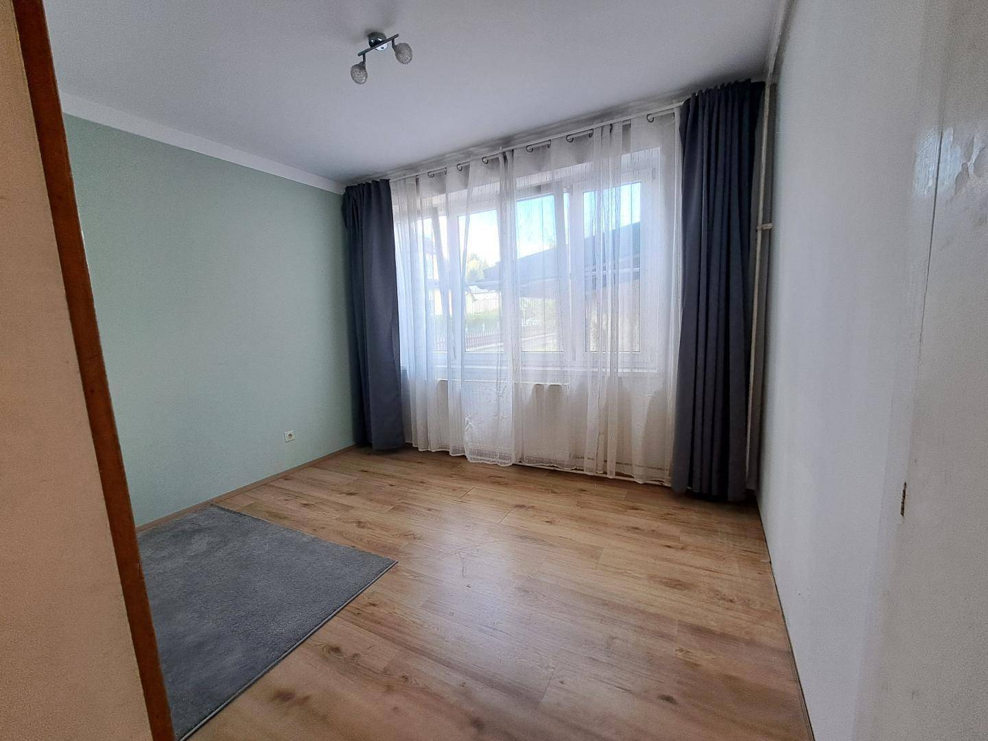 Schlafzimmer mit hellem Holzboden, großen Fenstern und einer Wand in sanftem Grünton.