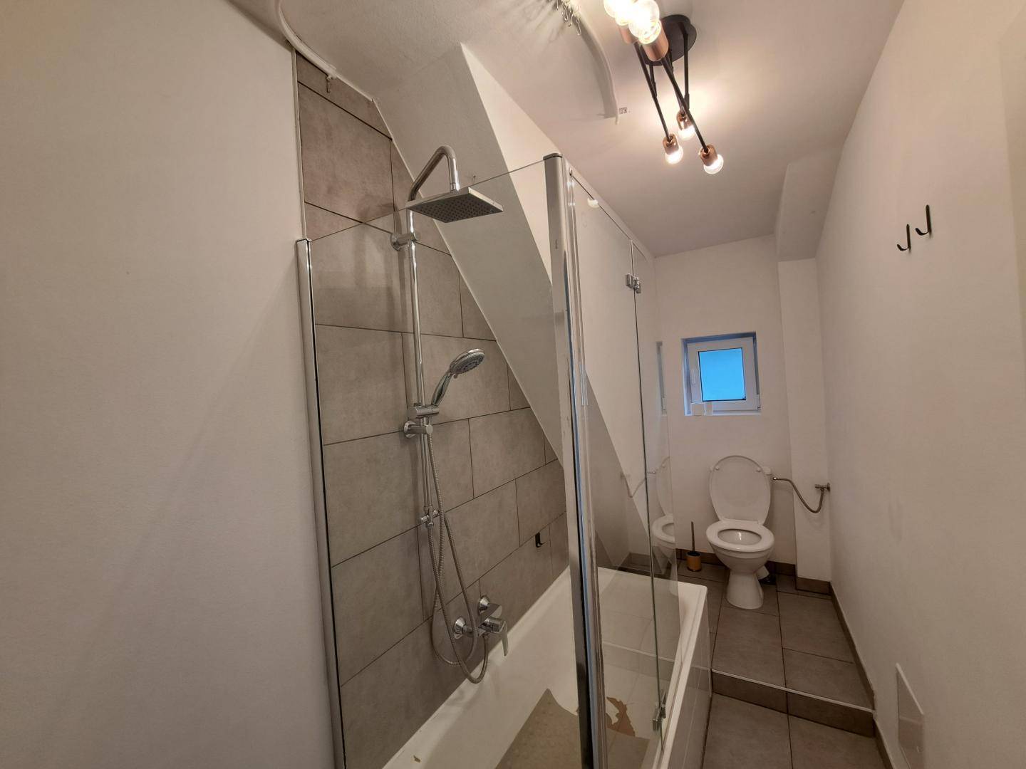 Modernisiertes Badezimmer mit Dusche über der Badewanne und Dachschräge.