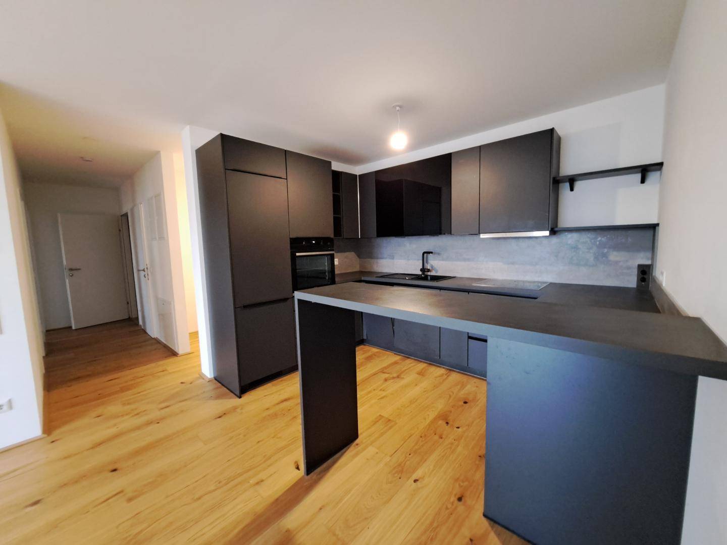 Moderne Küche mit dunklen Schränken, integrierten Geräten und Holzboden.