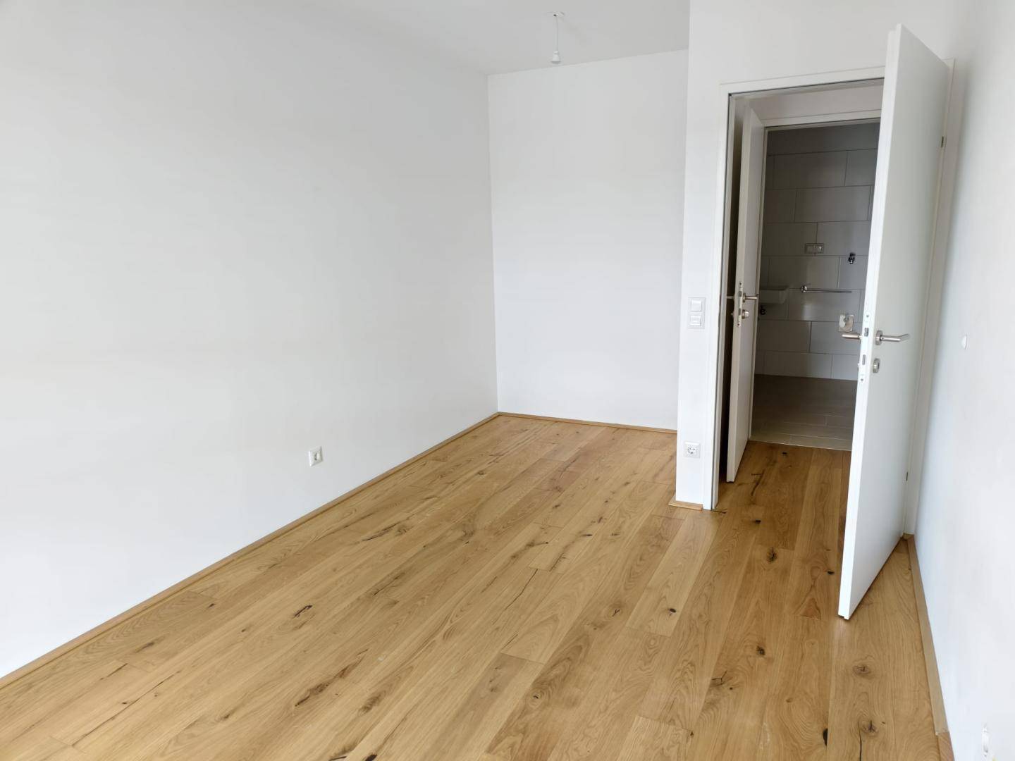 Leeres Zimmer mit Holzboden und direktem Zugang zu einem Badezimmer.