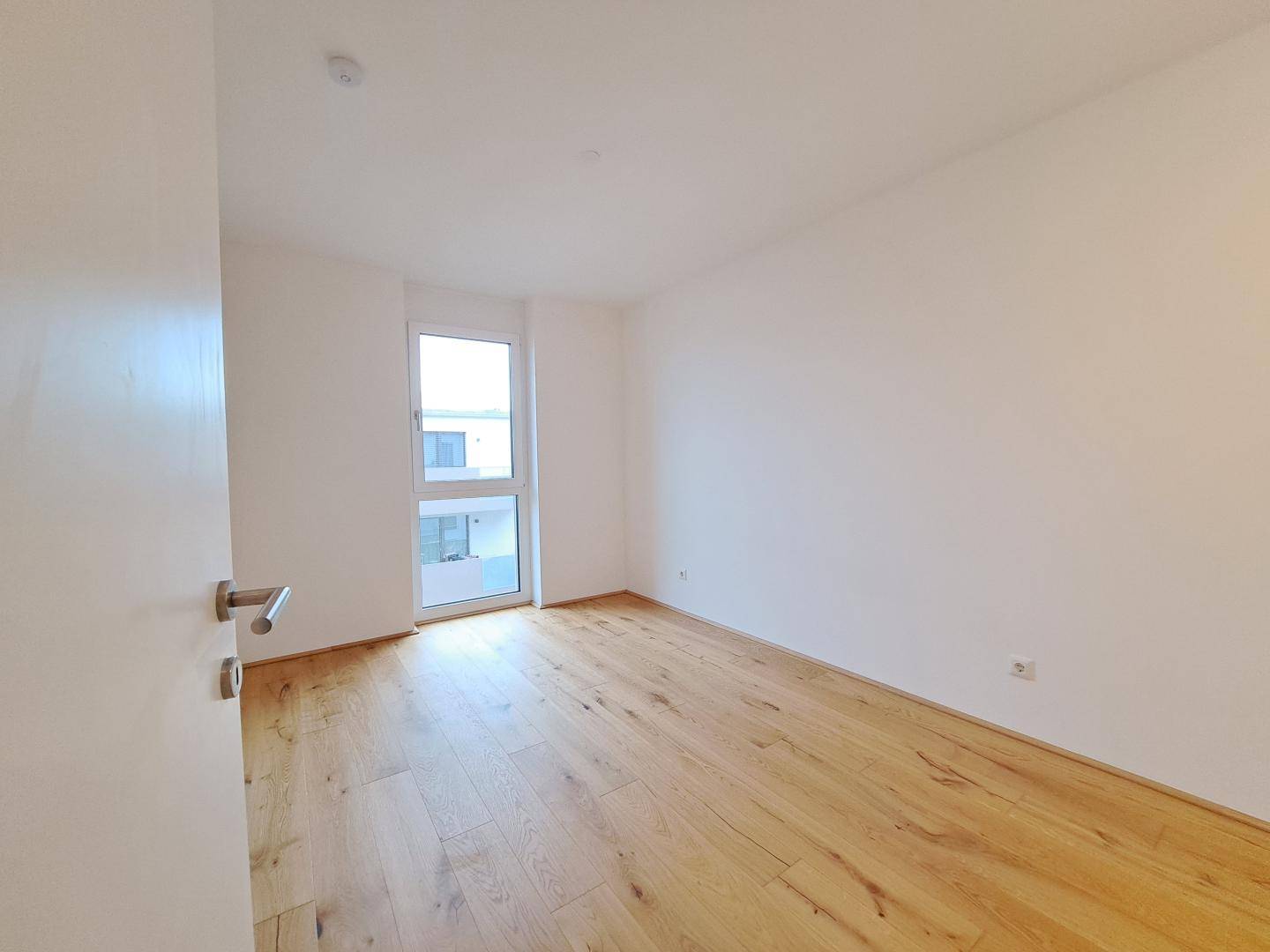 Helles Zimmer mit Holzboden und Fenster, bereit zur individuellen Gestaltung.