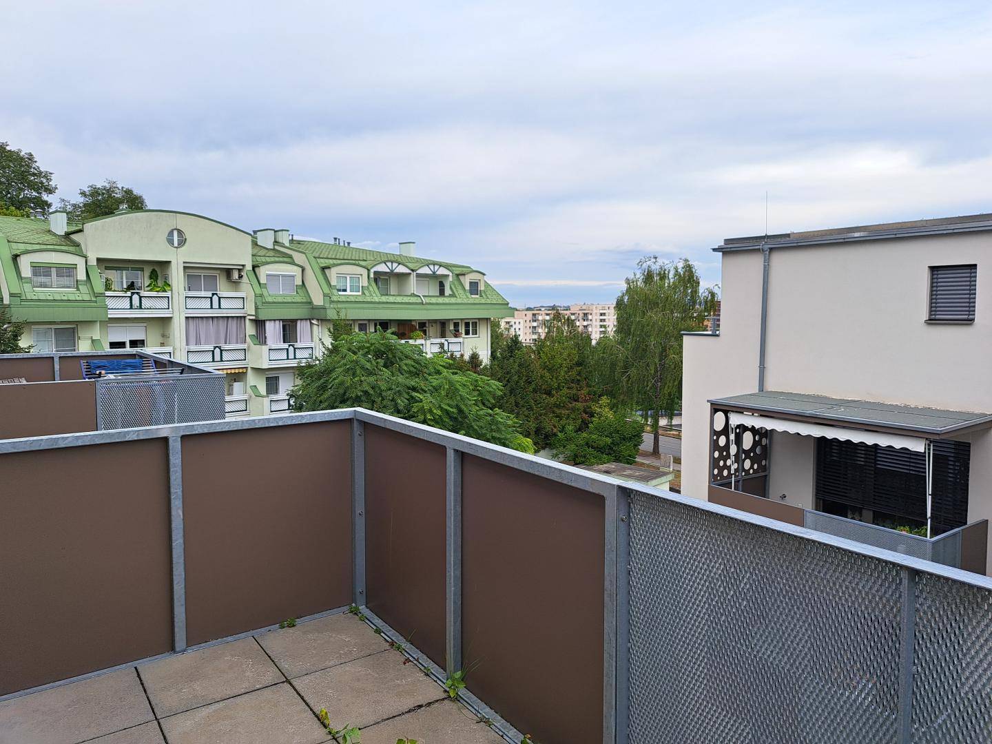 Blick von einem Balkon auf die umliegende Wohnbebauung und grüne Bäume.