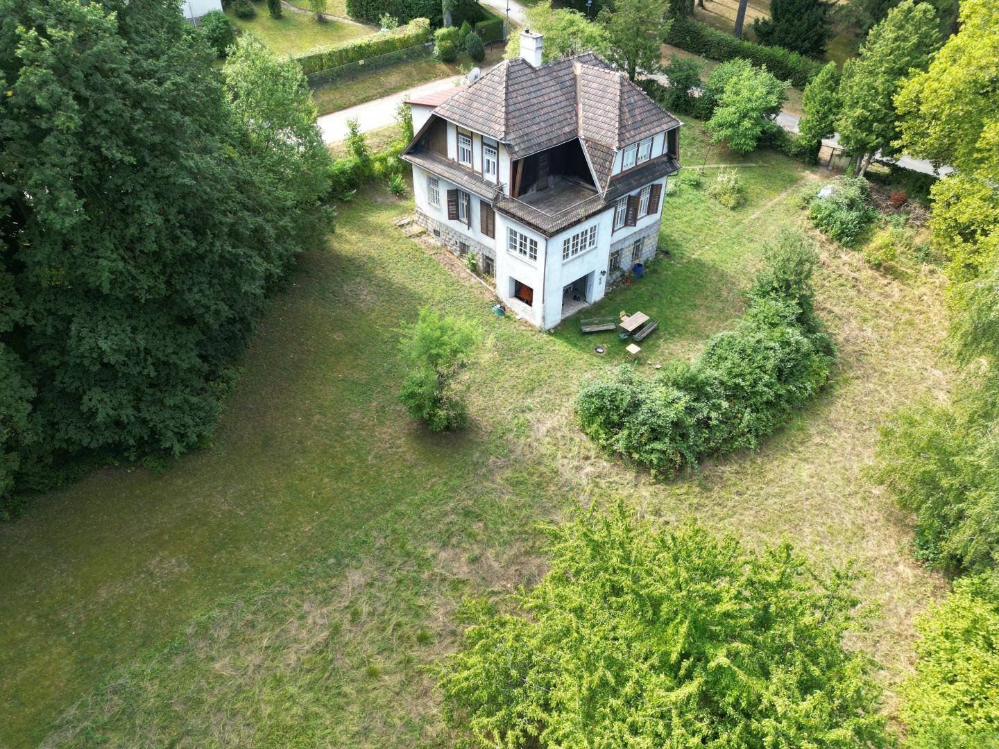 Luftaufnahme eines historischen Hauses mit weitläufigem Garten und altem Baumbestand.