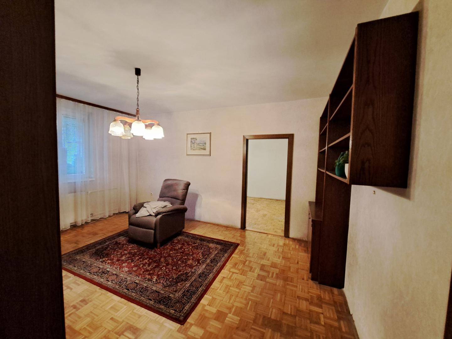 Wohnzimmer mit Parkettboden, Sessel und Blick in angrenzenden Raum.